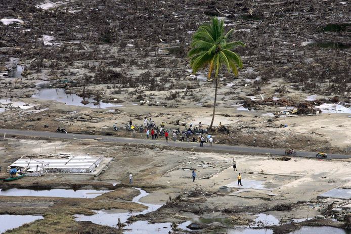 Slachtoffers van een tsunami schuilen onder een palmboom. De rest van het stadje is vernield.