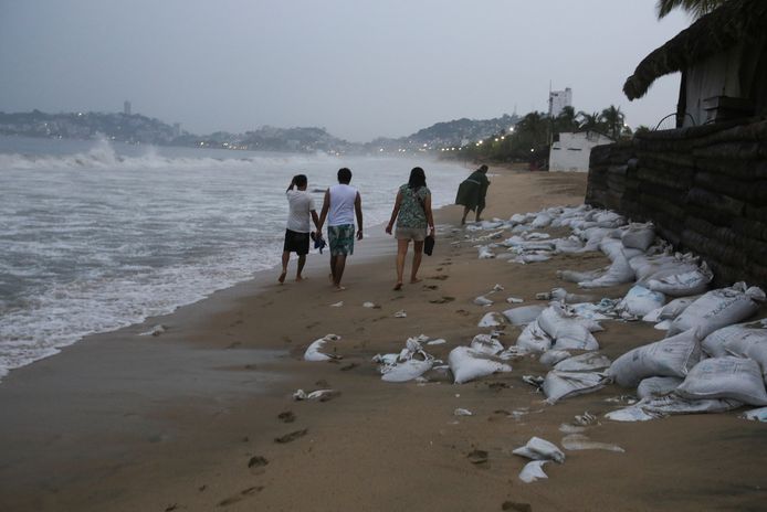 Mensen lopen langs een strand waar zandzakken liggen, terwijl orkaan Otis nadert.