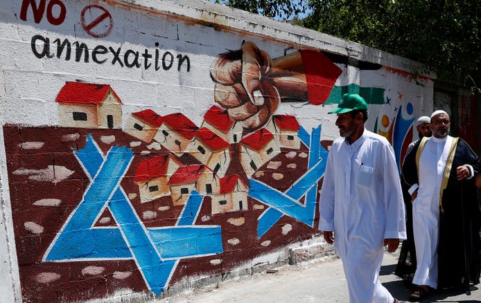 Hamas-aanhangers lopen langs een muurschildering die zich uitspreekt tegen Israëls annexatieplannen van de  Westelijke Jordaanoever.