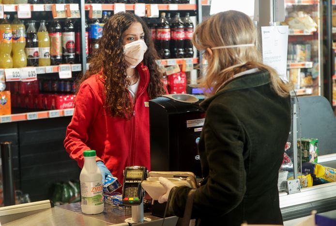 Een vrouw rekent haar boodschappen af bij de kassierster in een buurtsupermarkt in Napels.  Ze dragen beiden mondmaskers .