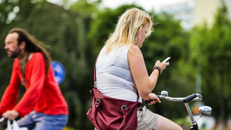 Een fietsster gebruikt haar mobiele telefoon op de fiets. Beeld anp