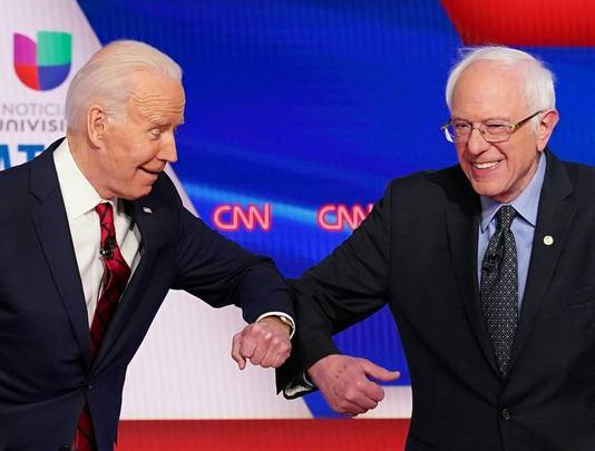 Joe Biden en Bernie Sanders schudden elkaar niet de hand, maar kiezen in deze coronatijden voor een veiligere begroeting.
