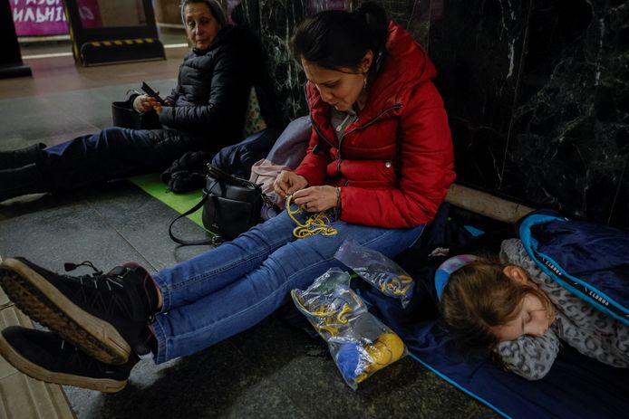 Een vrouw maakt pattriotistische armbandjes in de kleuren van de Oekraïense vlag, terwijl haar dochter in een metrosttaion van Kiev slaapt tijdens een nachtelijke Russische luchtaanval op de stad. (19/12/2023)