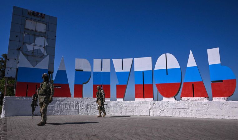 Russische soldaten lopen wacht op de plaats waar bezoekers verwelkomd worden in Marioepol. De letters zijn geschilderd in de kleuren van de Russische vlag. Beeld AFP
