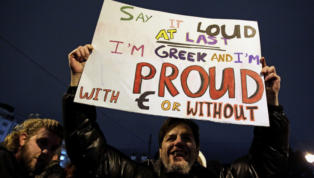 Archieffoto van een protest in Athene waarbij een demonstrant een bord omhoog houdt. 'Ik zeg het eindelijk hardop. Ik ben Griek en trots met euro of zonder.' Beeld epa