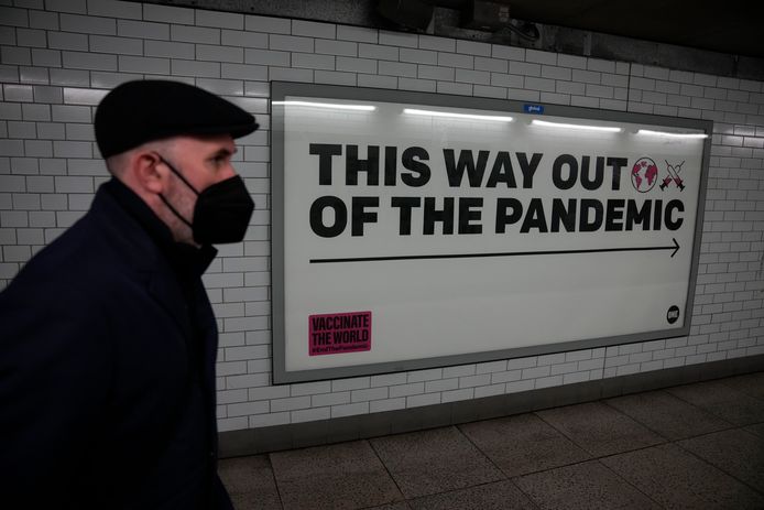 Een man met een mondmasker loopt langs een poster in de metro van Londen