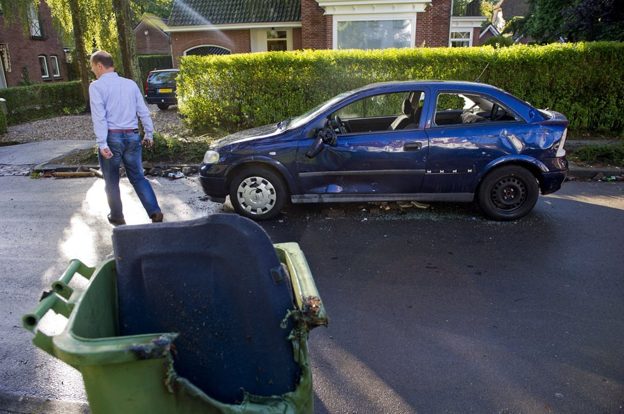 Een gesloopte auto en een vuilcontainer staan op de Stationsweg in Haren.