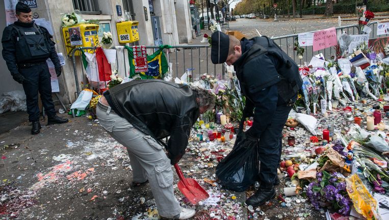 Parijs: twee mannen onder wie een politieagent halen waxinelichtjes en resten rouwmateriaal weg bij de ingang van popconcertzaal Le Bataclan, waar vrijdagavond zeker 89 mensen de dood vonden. Beeld Getty Images