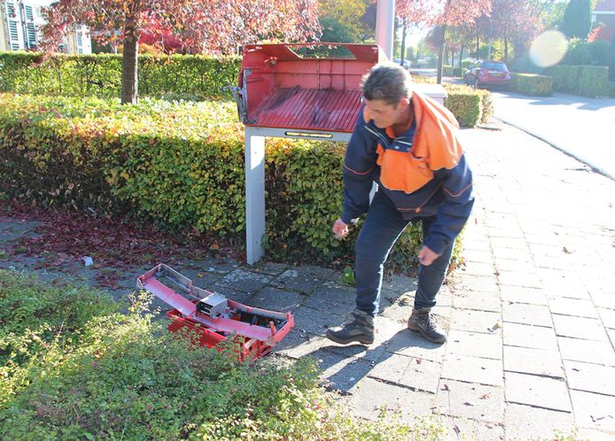 Een medewerker van PostNL verzamelt de brokstukken van de vernielde brievenbus.