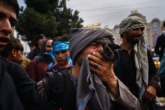 Mannen kijken ontsteld toe hoe de taliban mensen met stokken, zwepen en zelfs wapens bewerken terwijl ze het luchthaventerrein in Kaboel willen betreden om het land te ontvluchten.