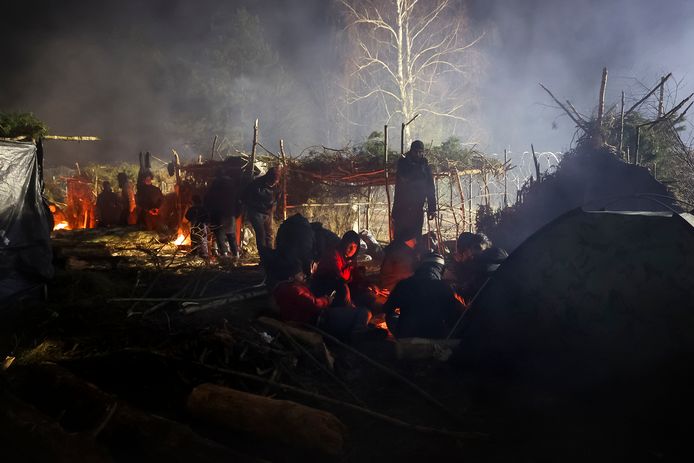 Vluchtelingen verwarmen zich aan een vuurtje in een geïmproviseerd tentenkamp aan de grens tussen Wit-Rusland en Polen.
