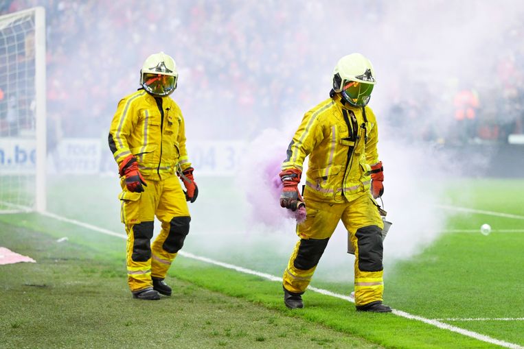 Twee brandweermannen verwijderen rookbommen in Luik. De wedstrijd tussen Standard en Anderlecht is gestaakt wegens wangedrag van de bezoekende supporters. Beeld Photo News