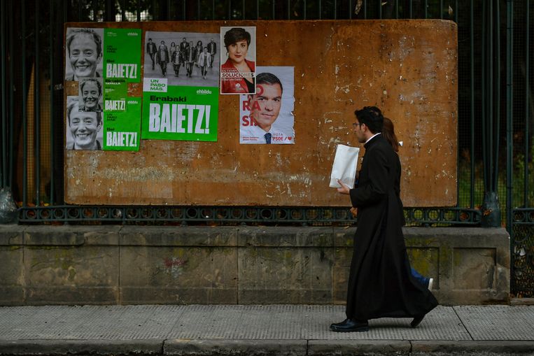 Een Spaanse priester loopt langs een muur met verkiezingsposters in het Noord-Spaanse Tafalla. Afgelopen zondag waren de vierde verkiezingen in vier jaar.  Beeld AP