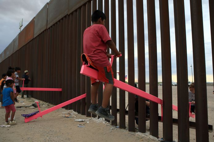 Amerikaanse en Mexicaanse families spelen op een wip die tussen de spijlen van een grenshek is bevestigd.