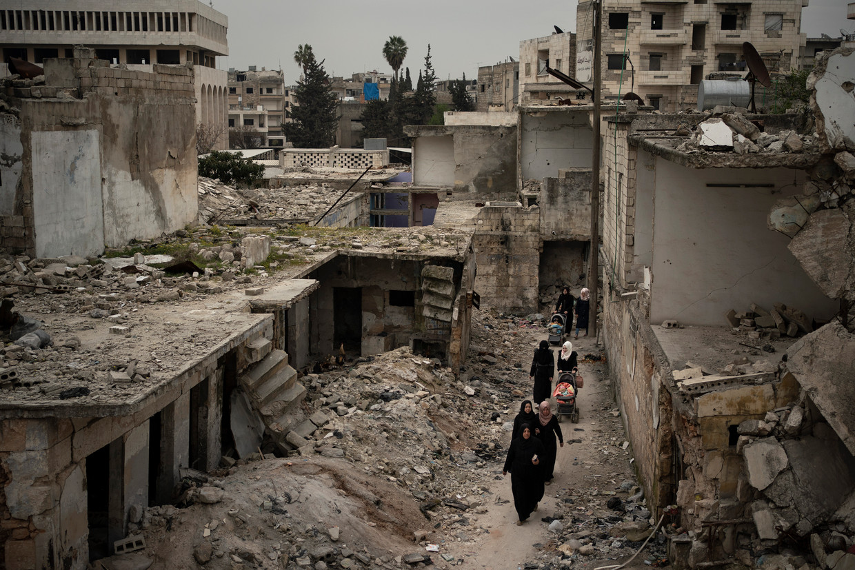 Vrouwen lopen door een zwaarbeschadigde wijk in Idlib, Syrië in maart vorig jaar. Beeld AP