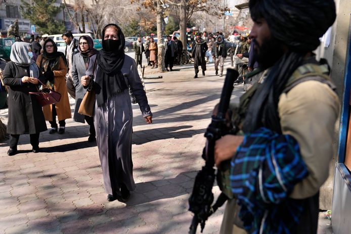 Een Afghaanse vrouw wandelt voorbij een talibanstrijder in de Afghaanse hoofdstad Kaboel.