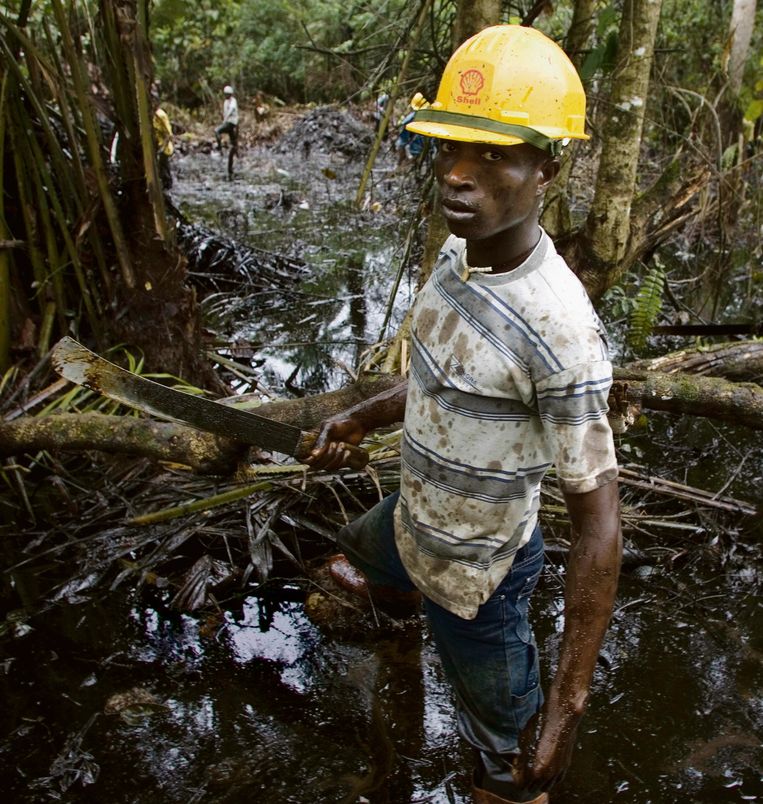 Een door Shell ingehuurde medewerker helpt bij het opruimen van olievervuiling bij een put in de Nigerdelta.  Beeld Ed Kashi