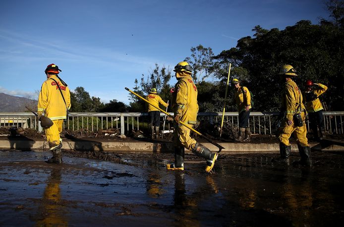 Brandweermannen lopen op een met modder besmeurde weg in Montecito, Californië.