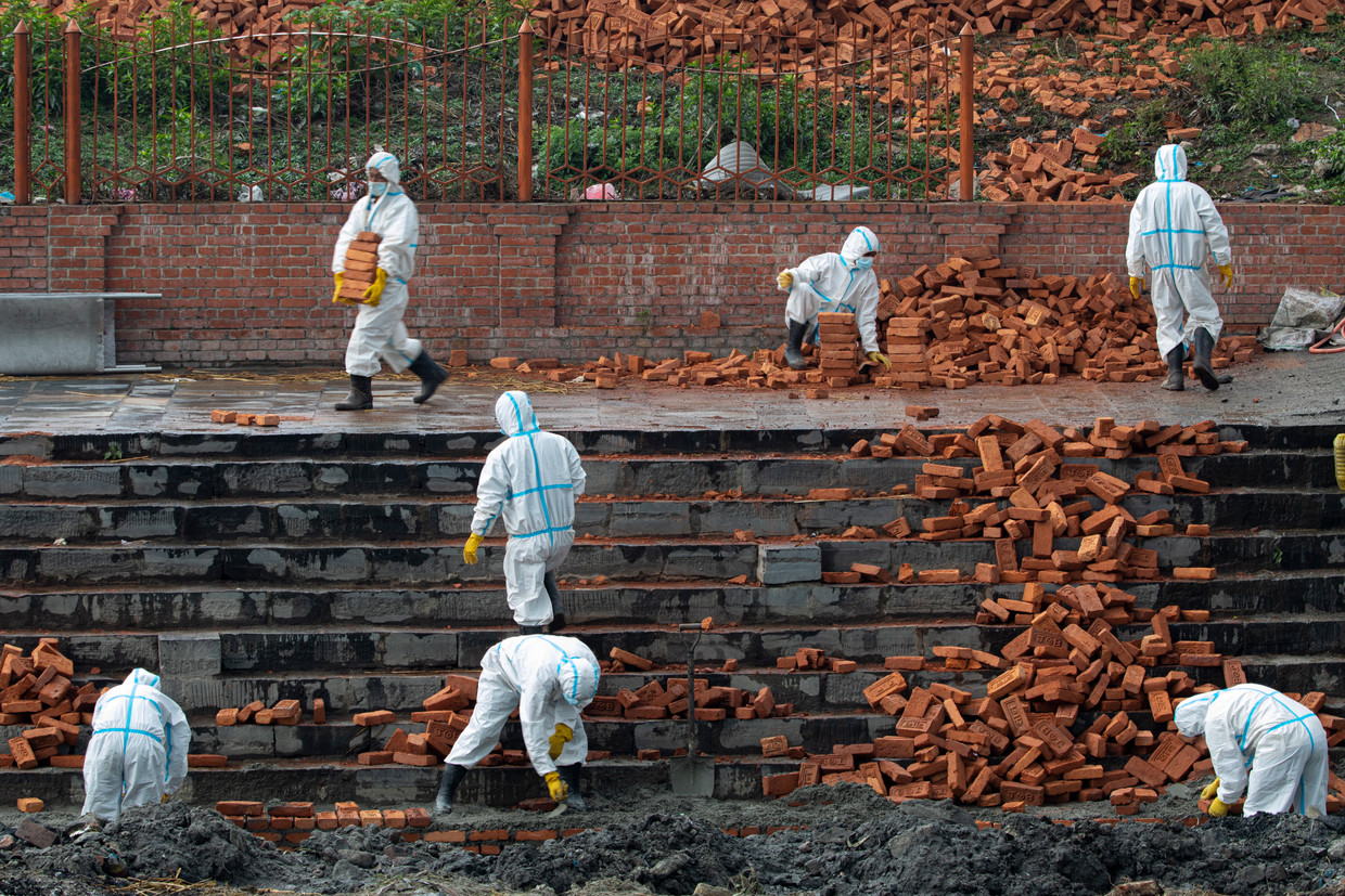 Nepalese werknemers in beschermende pakken breiden een crematorium uit in hoofdstad Kathmandu. Het land ziet het aantal doden door de coronacrisis toenemen.  Beeld EPA