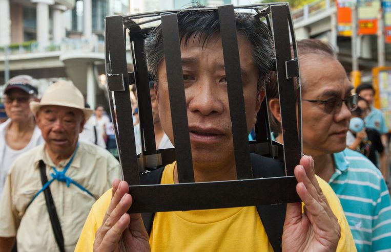 Een demonstrant draagt een kooi op zijn hoofd als protest tegen de  tegen de celstraffen voor activisten Joshua Wong, Nathan Law en Alex Chow. De drie werden vorige week wegens hun leidende rol in de massabetogingen in 2014 veroordeeld tot gevangenisstraffen tussen de zes en acht maanden. Beeld EPA