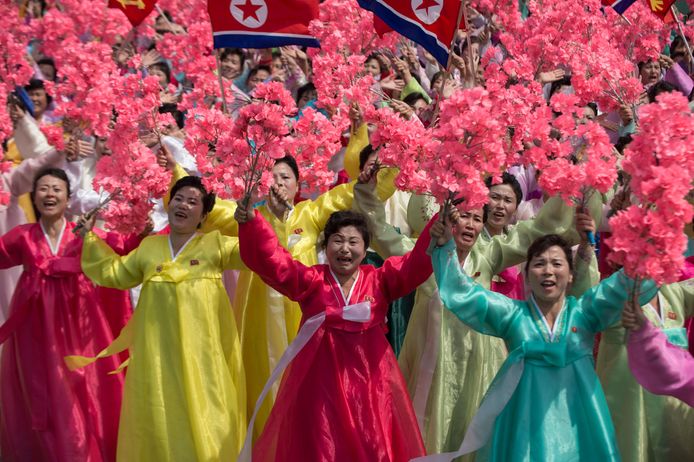 Vrouwen in traditionele kleurrijke Koreaanse jurken zwaaien met bloemen terwijl de leider Kim Jong-un passeert.