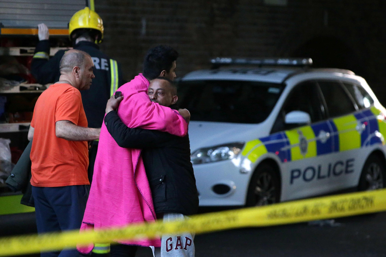 Twee mannen sluiten elkaar in de armen binnen het afgesloten gebied rond de Grenfell Tower. Beeld AFP