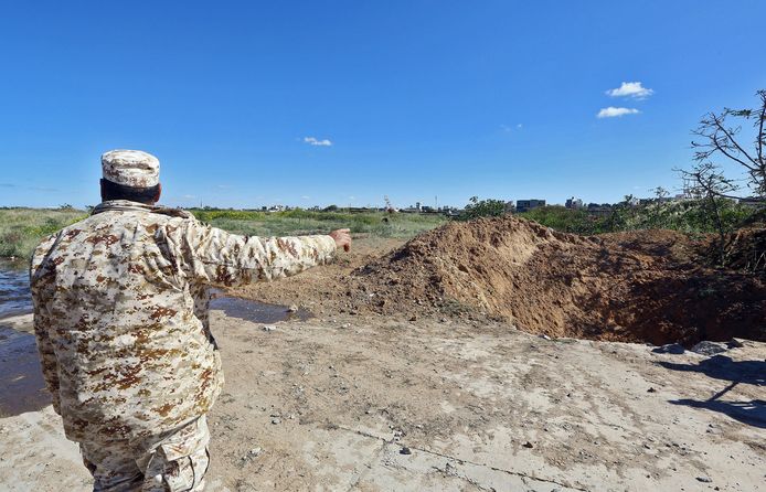 Een Libische veiligheidskracht wijst naar een krater waar vorig jaar in april een raket insloeg in de luchthaven.