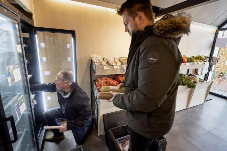 Varkensboer Tonnie Veldhuis (links) vult de schappen in de onbemande winkel in Wilp. Initiatiefnemer Lukas Lagerweij biedt een helpende hand.  Beeld Herman Engbers