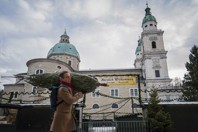 Beeld van afgelopen woensdag. Een man wandelt met een kerstboom voorbij een gesloten kerstmarkt in Salzburg tijdens de lockdown in Oostenrijk.