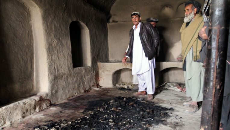 Mannen staan naast bloedvlekken en verbrande resten in een huis waar volgens ooggetuigen Afghanen zijn vermoord door Amerikaanse soldaten. Beeld AP