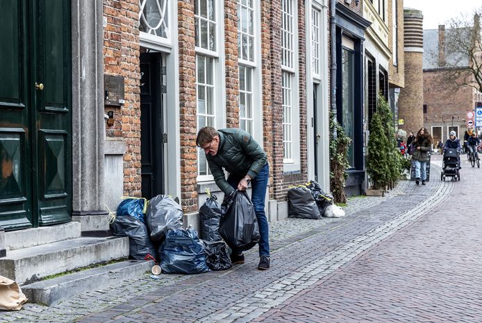 Een bewoner van de Oudegracht ordent de stapel vuilniszakken voor zijn deur.
