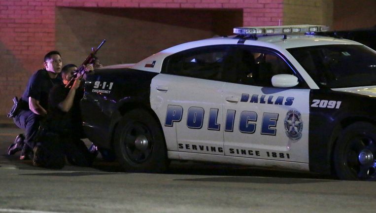 De politie schuilt achter een politie-auto in Dallas. Beeld ap