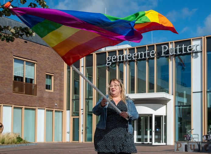 Christa Koekoek zwaait de regenboogvlag bij het gemeentehuis in Putten. Ze wil dat de gemeente de regenboogvlag hijst op Coming Out Day.