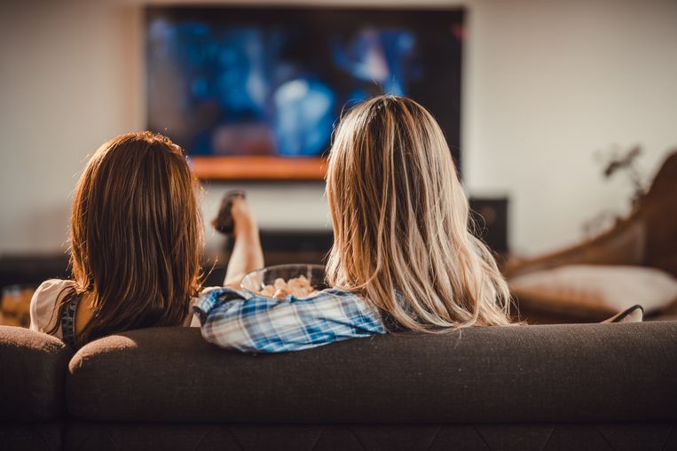 Back view of female friends watching TV on sofa at home. Beeld Getty Images/iStockphoto