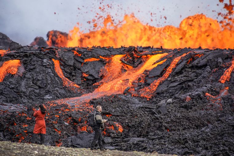 Mensen kijken van dichtbij naar de lava die uit de Fagradalsfjall op IJsland stroomt. De vulkaan, 32 kilometer ten zuidwesten van hoofdstad Reykjavik, is nog geen acht maanden na de laatste eruptie opnieuw tot uitbarsting gekomen. Beeld AP