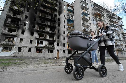 Archiefbeeld. Twee jong vrouwen wandelen met een kinderwagen voorbij een vernietigde woonblok in de Oekraïense stad Tsjernihiv. (Foto 3 mei 2022)