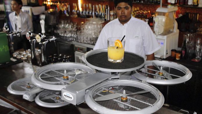 Een barman kijkt toe hoe een vliegende robot zijn drankjes naar de juiste tafel brengt.