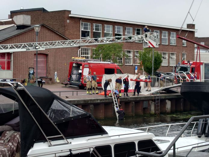 Brandweerlieden en politie zijn bezig om de overleden persoon uit het water te tillen.