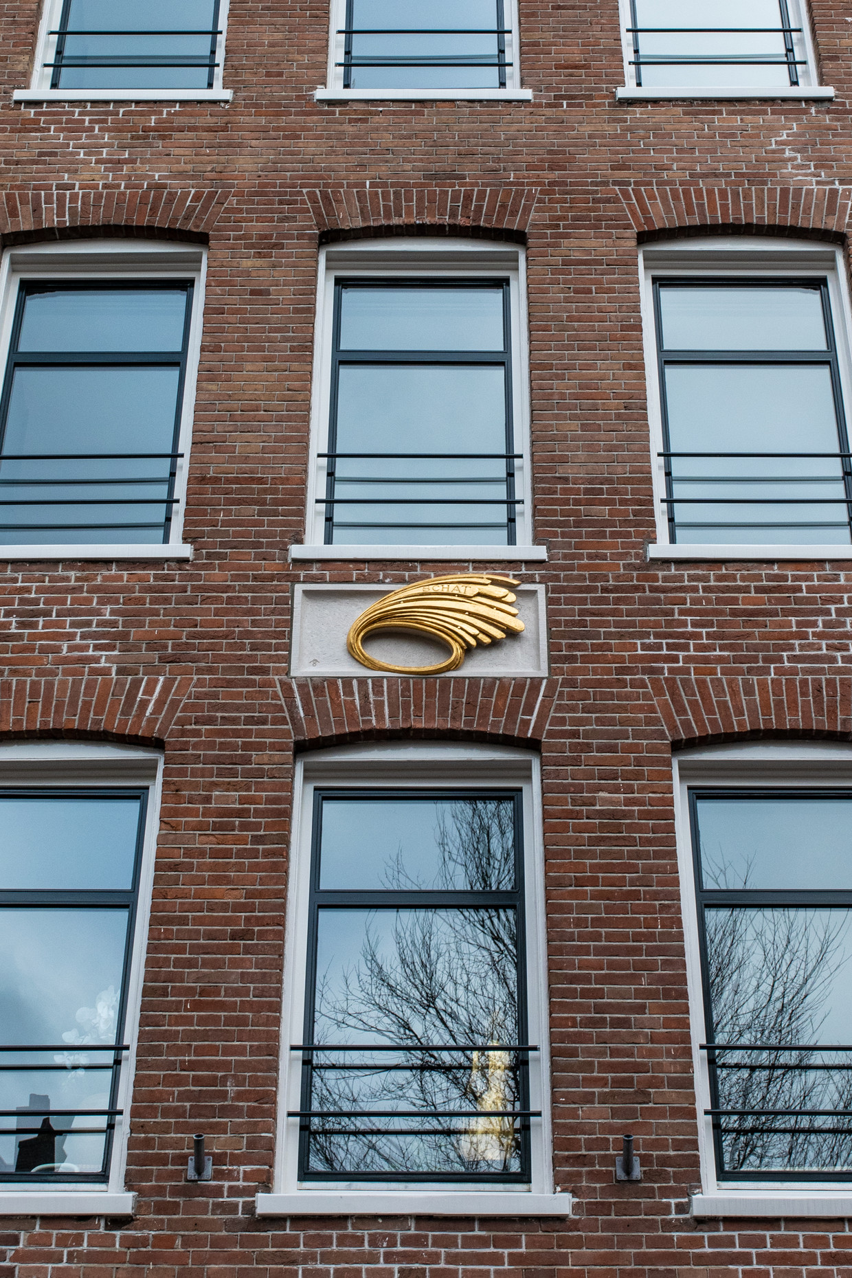 De gevelsteen is een goud-witte, gevederde steen met daarop ‘SCHAT 1960-2020.’ Gouden windveren zijn een van de handelsmerken van sieradenontwerper Anneke Schat. Beeld Nosh Neneh