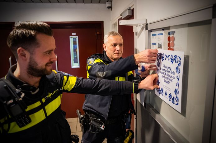 Wijkagent Jacques Lems (r.) plakt een poster in de hal van een flat, met een tekst die bewoners moet waarschuwen tegen onverlaten die met een smoesje hun woning willen binnenkomen. 'Zeker op oudere personen heeft dit een grote impact'.