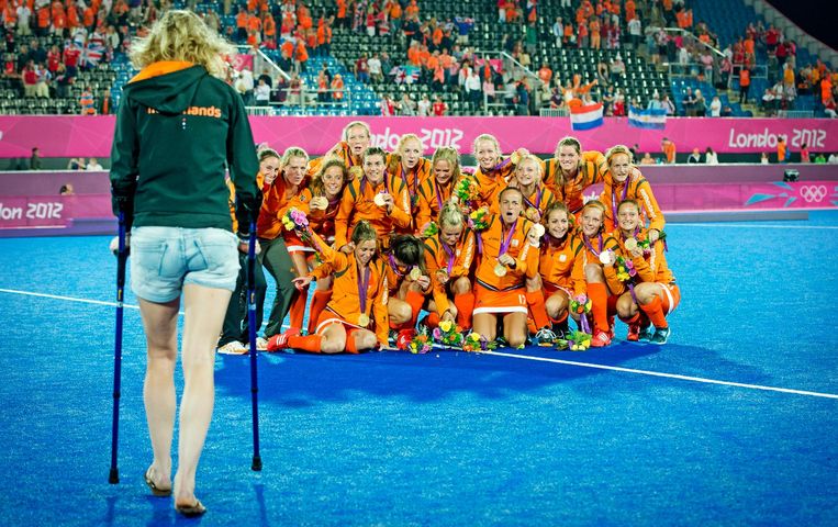 De geblesseerde Willemijn Bos loopt naar Nederlandse hockeydames die hun gouden medaille vieren na de gewonnen finale tegen Argentinië op de Olympische Spelen in Londen. Beeld anp
