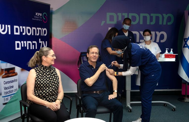 President Isaac Herzog (midden) ontvangt een derde prik tegen het coronavirus. In Israël komt een campagne op gang om zestigplussers een 'boosterprik' te geven.  Beeld EPA