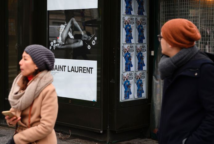 Winkelend publiek in Parijs passeert een van de reclameposters van Yves Saint Laurent.
