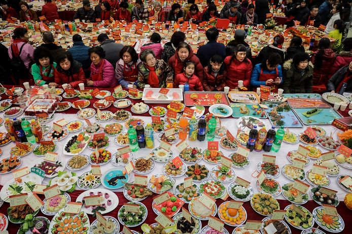 Chinese buurtbewoners in Wuhan zitten rond grote tafels waarop huisgemaakte gerechten staan uitgestald. De wijkbewoners koken bij het begin van het nieuwe jaar duizenden gerechten en nodigen de buren uit om te proeven en te leren van de kookvaardigheden van anderen. Foto Wang He