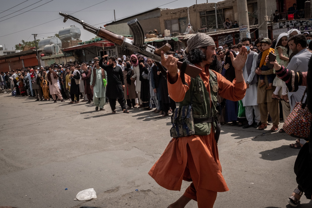 Een talibanstrijder drijft hardhandig mensen terug aan het vliegveld van Kaboel. Beeld Jim Huylebroek for The New York Times