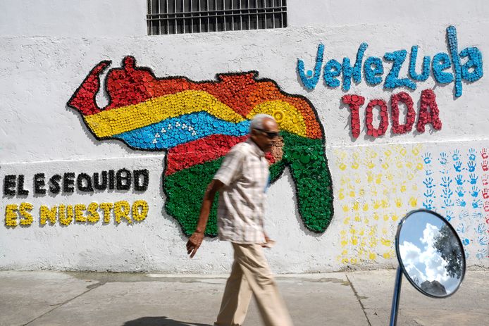 Een man loopt langs een muurschildering in de Venozolaanse hoofdstad Caracas, waar links “Essequibo is van ons” staat.