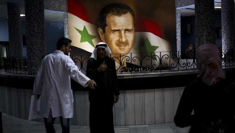 Mensen wandelen langs een portret van president Bashar al-Assad in een ziekenhuis in Damascus. Beeld ap