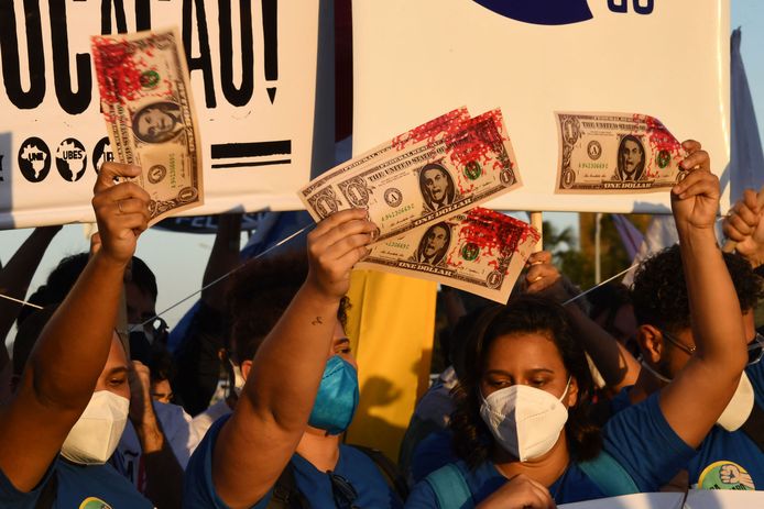 Demonstranten hadden met rode verf besmeurde nepdollarbiljetten meegenomen. Een dollar is de vermeende meerprijs die het ministerie vroeg per dosis van het vaccin.