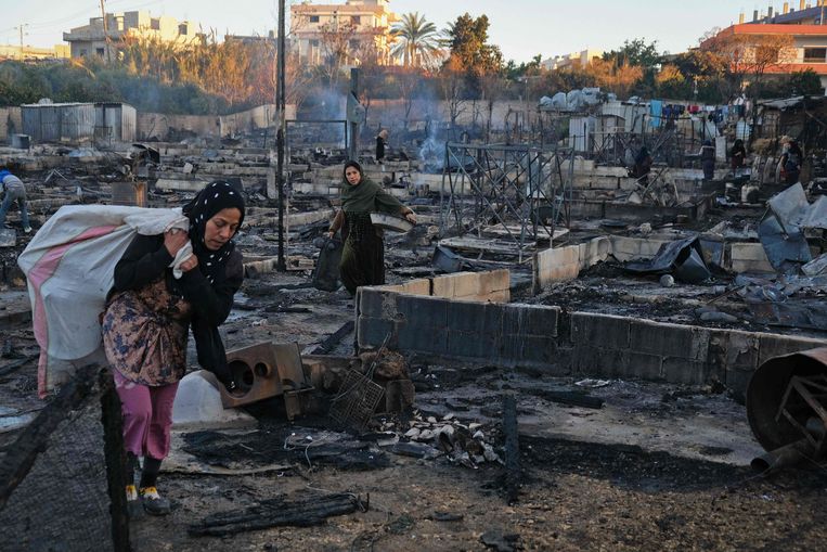Syrische vluchtelingen in de Libanese provincie Minja zoeken naar hun eigendommen in de smeulende resten van het kamp dat in brand werd gestoken. Beeld AFP