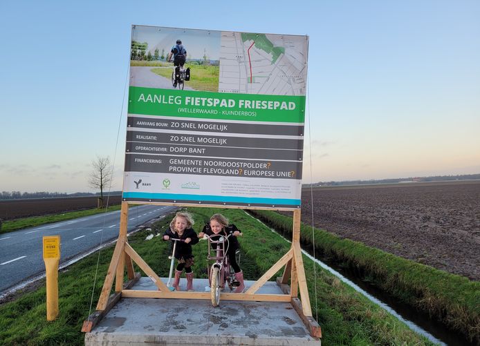 De kinderen van Wietze van Wegen bij het ludieke bouwbord, op de plek waar ze hopen dat binnenkort een fietspad ligt.